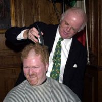 gentleman in a suit shaving another gentlemans hair